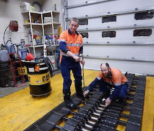 Two expeditioners tensioning bolts on a snow groomer track.