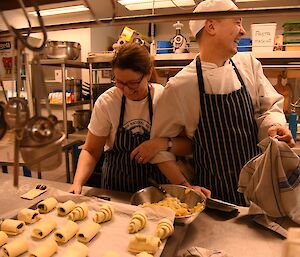 Two expeditioners standing at a kitchen bench behind a pastry tray.