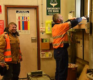 Two expeditioners standing near a window, working on a piece of satellite communications.