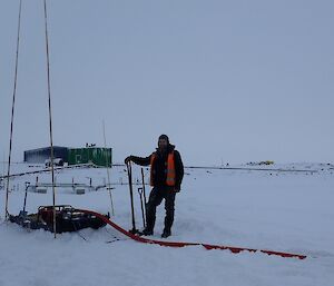 Expeditioner standing shovel in hand next to a water pump and generator with a green building in the background