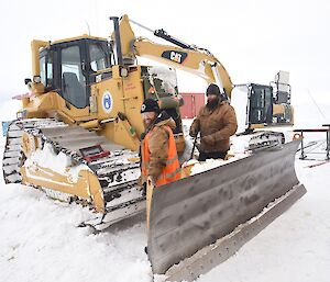 Two expeditioners face camera standing next to a bulldozer