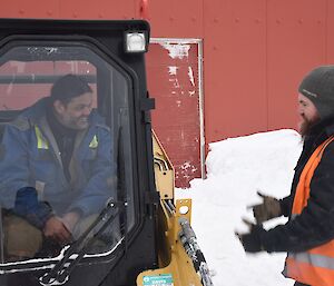 Two expeditioners, one in a skid steer share a smile
