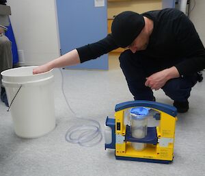 Expeditioner checking the suction on a portable suction unit as he kneels beside a bucket in an operating theatre