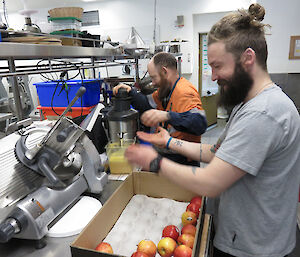 Two expeditioners standing in profile work feeding apples into a juicer