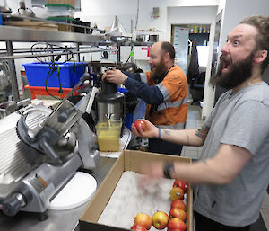 Expeditioners in profile with excited expressions on their faces juicing apples in a juicer