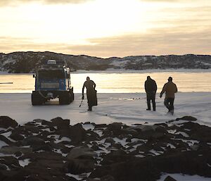 Three expeditioners walking back to the tracked vehicle silhouetted by brilliant golden sunshine