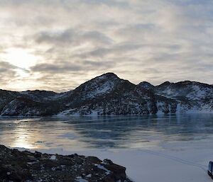 Panoramic photo of a frozen lake and rocky hills with a tracked vehicle in bottom right of frame