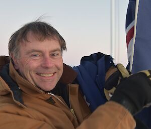 Expeditioner smiling at camera holding an Australian flag in his hand