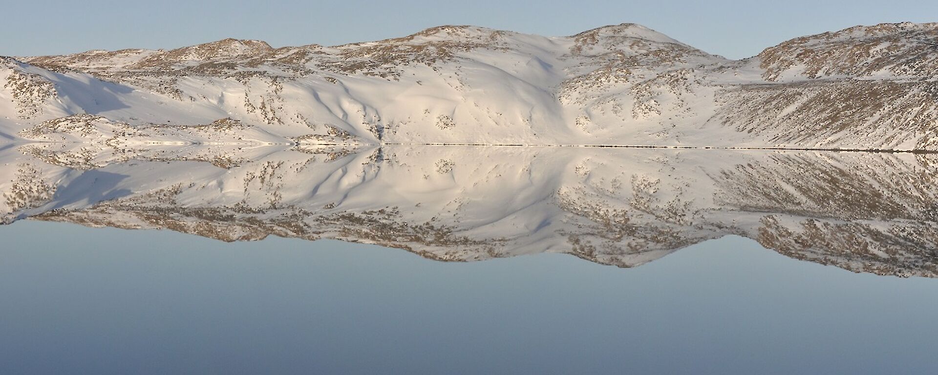 Panoramic photo of a calm lake with snow covered hills surrounding it