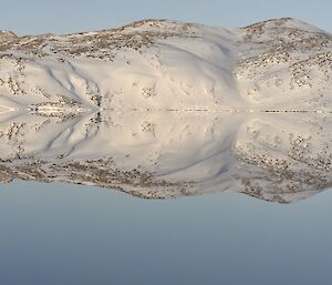 Panoramic photo of a calm lake with snow covered hills surrounding it