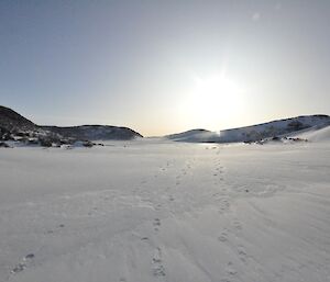 Three pairs of footprints in the snow lead through a valley with snow covered hills on either side