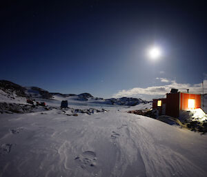 Night time shot of a red field hut with the moon shining above it