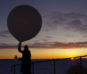 Expeditioner and illustration cut out silhouetted by the sun, about to release a weather balloon