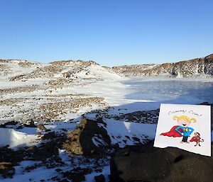 Illustration propped against a rock with frozen lake and snow covered hills in background