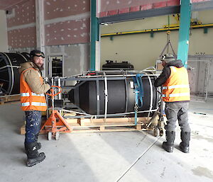 Two expeditioners moving heavy equipment inside a large storage area
