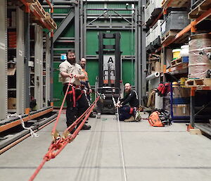 Three expeditioners standing attached to ropes in an aisle of the storage warehouse