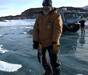 Expeditioner standing over an electric drill on a frozen lake