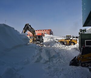 Mechanical digger and a bulldozer clearing snow next to a large snow rise