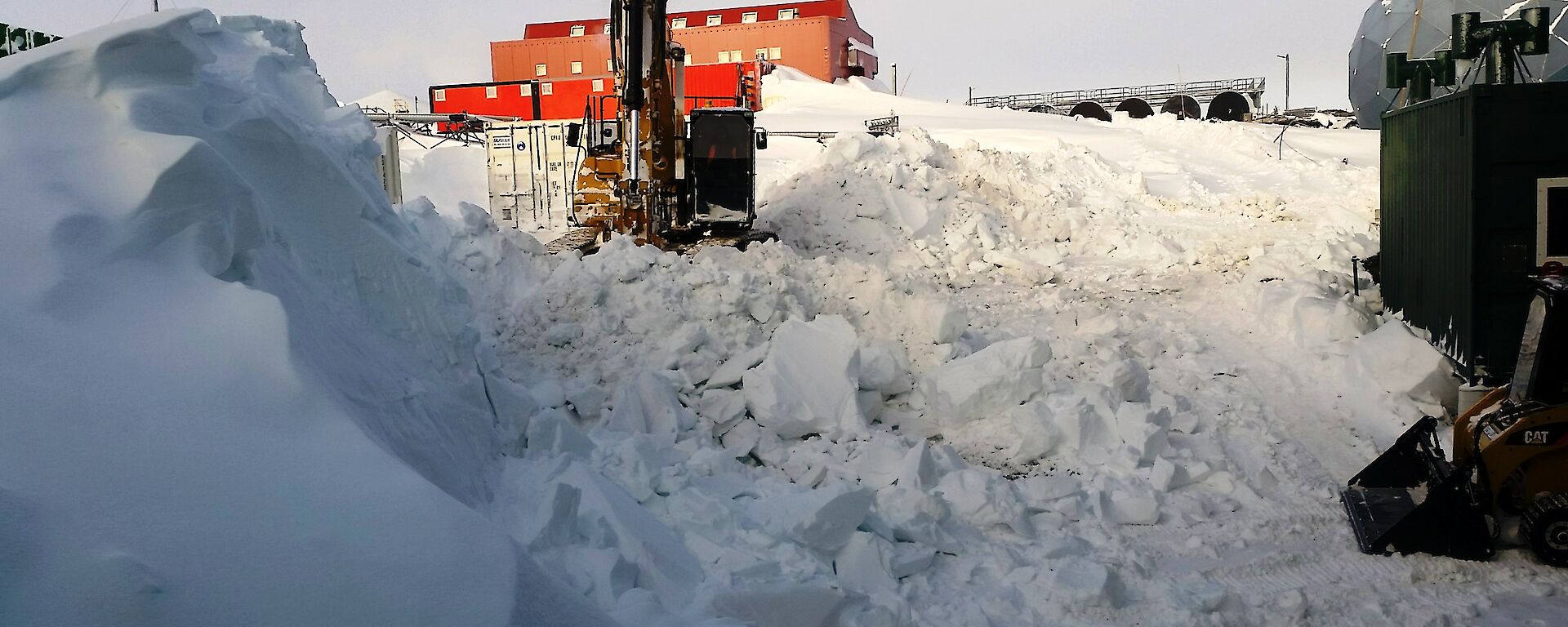 Excavator clearing snow in background with large build up of snow in foreground
