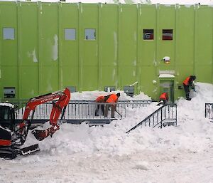 A team of expeditioners shovelling snow in front of a large green building