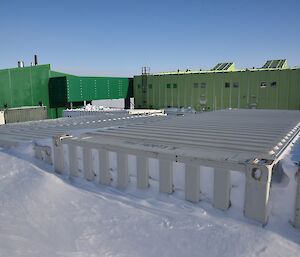 20 feet long shipping containers buried in snow in foreground. Large green building in background