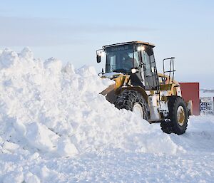 Expeditioner driving a mechanical loader pushing a large mound of snow