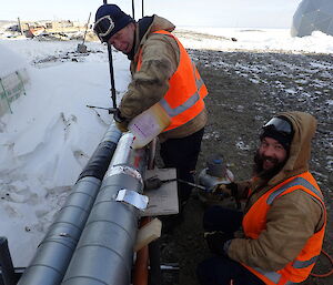 Two expeditioners standing over a pipeline