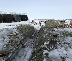 Expeditioners in background walking beside an excavated culvert with exposed piping