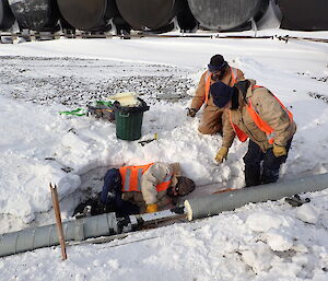 Three expeditioners kneeling over exposed pipe work