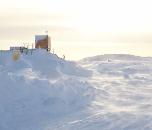 winds dusting loose snow across the surface. Cargo containers and a heli pad in background