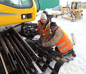 Two expeditioners kneeling in front of a snow grooming track