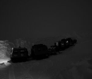 Two tracked vehicles with sleds on making their way down along the road off station in the darkness