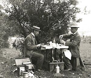 Vintage photo of two men having an outdoor picnic with table