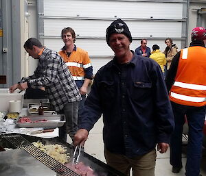 Expeditioner standing beside a BBQ facing camera with other expeditioners in background