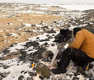 Expeditioner hunched over a camera on a tripod with rocky terrain in background