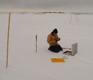 Expeditioner kneeling beside some scientific instrumentation