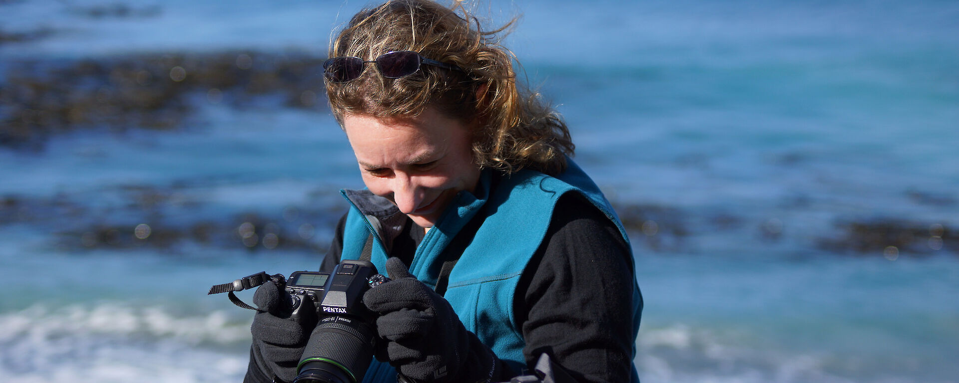 Expeditioner in foreground with head down smiling with sea in background