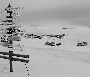 Davis signpost with many destinations in foreground. Two tracked vehicles in convoy crossing over snow covered ground in background