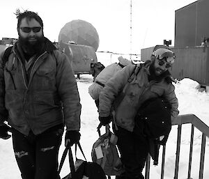 Two expeditioners dressed in cold weather attire smiling upon return to station