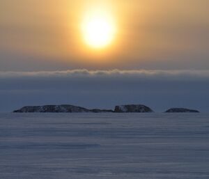 Sun hanging above clouds over the horizon above sea ice
