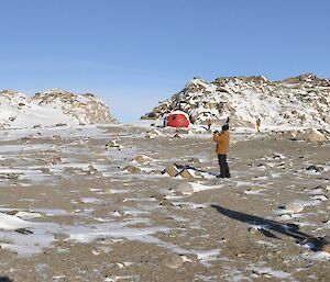 Panoramic photo of rocky terrain and snow with a red apple hut in background