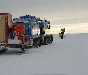 Expeditioner walking in front of a tracked vehicle on icy terrain