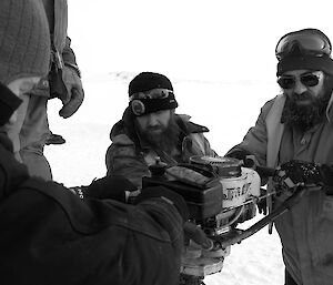 Three expeditioners operating a drill into the sea ice