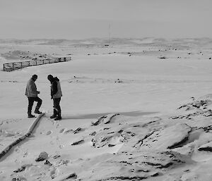 Two expeditioners in background inspecting a water hose out onto a frozen lake