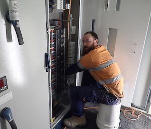 Expeditioner seated on a white bucket facing an electronics control board