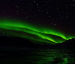 Green aurora in night sky reflected over frozen lake ice