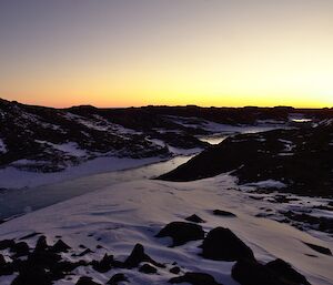 Sunset on horizon with snow covered rocky landscape