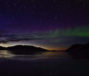 Frozen sea ice reflecting twilight sky with a green aurora