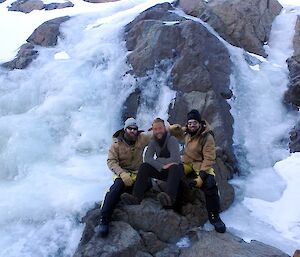 Two expeditioners with a third comically photoshopped in the middle seated in front of a frozen waterfall