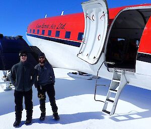 Two expeditioners pose beside a cargo plane on an ice plateau